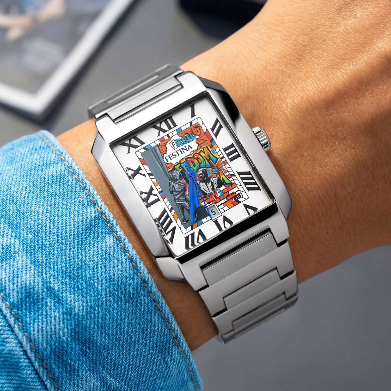 Festina Freedom 36 mm lifestyle wrist shot — hand-painted rectangular dial with street-art “FREEDOM” lettering and geometric color accents, paired with a brushed and polished stainless-steel bracelet. Limited edition by IFL Watches.