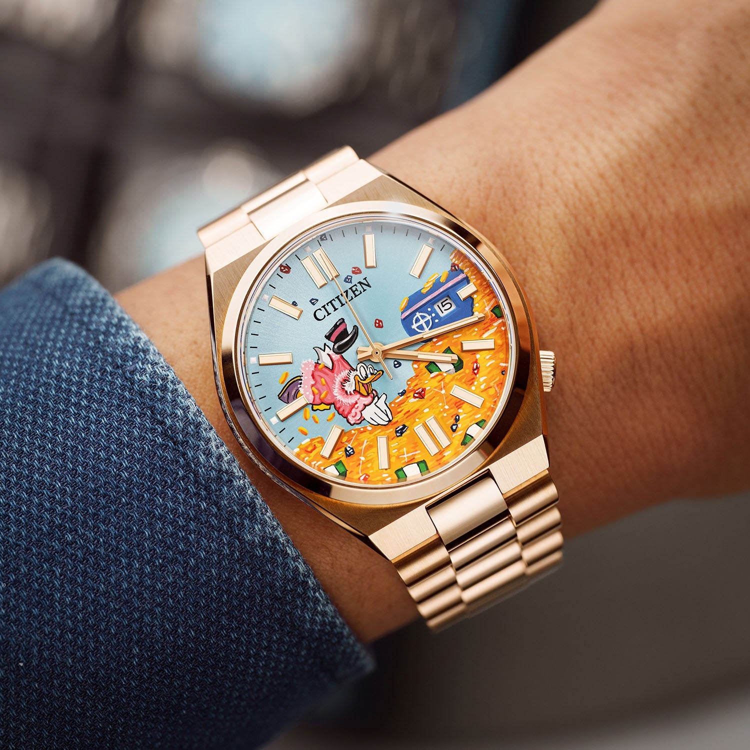 Citizen Tsuyosa Dive in Time on wrist — hand-painted dial showing a distinguished character diving into a pile of golden treasure, worn against a blue textured sleeve on a rose gold-plated case and bracelet, a bespoke timepiece by IFL Watches.